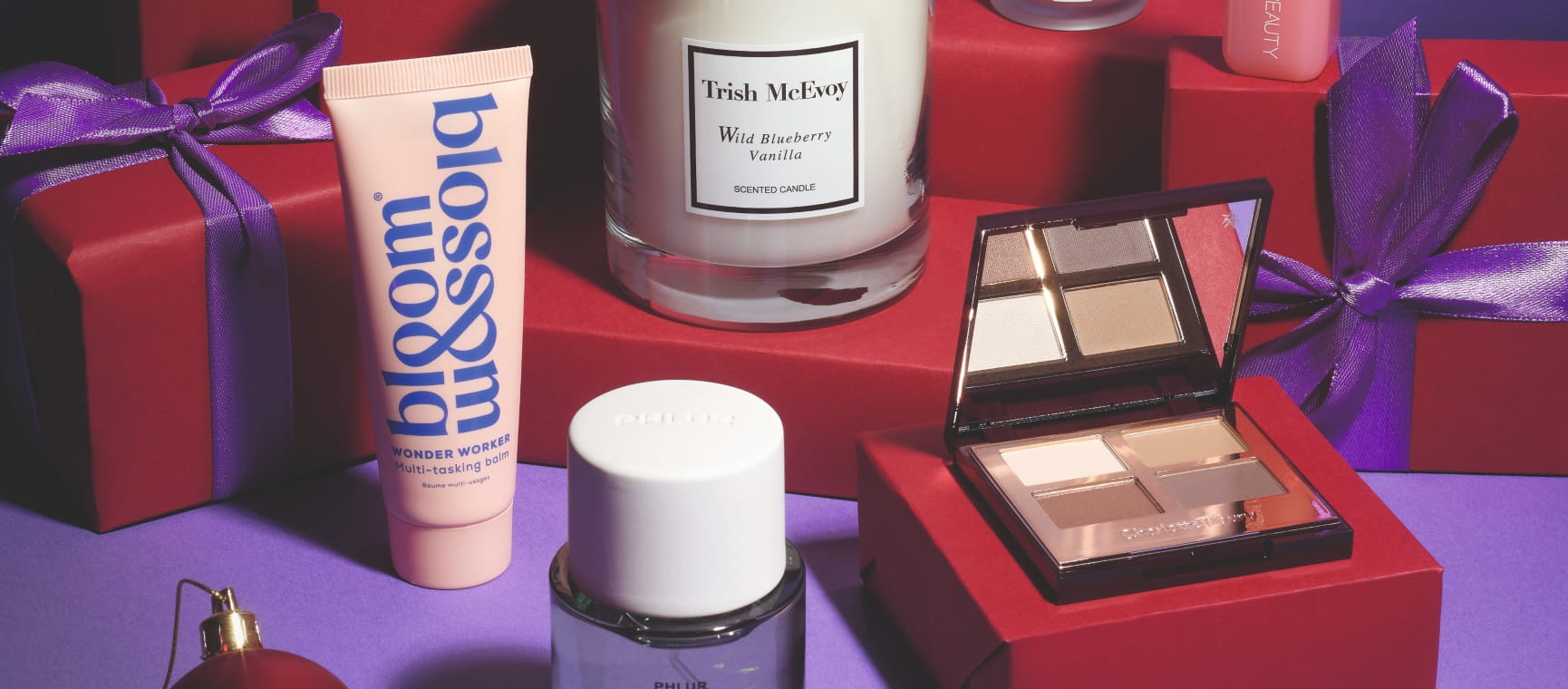 Beauty products including lip balm, eye shadow and a scented candle styled with red gift boxes