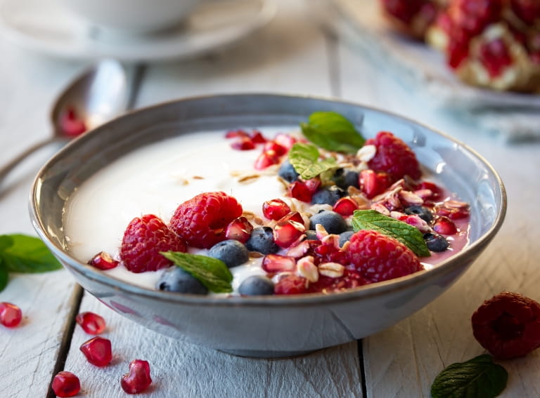 A bowl of yoghurt topped with blueberries, raspberries, pomegranate seeds and oat flakes