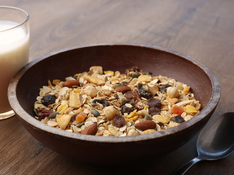 A brown bowl of muesli with a glass of milk on the side
