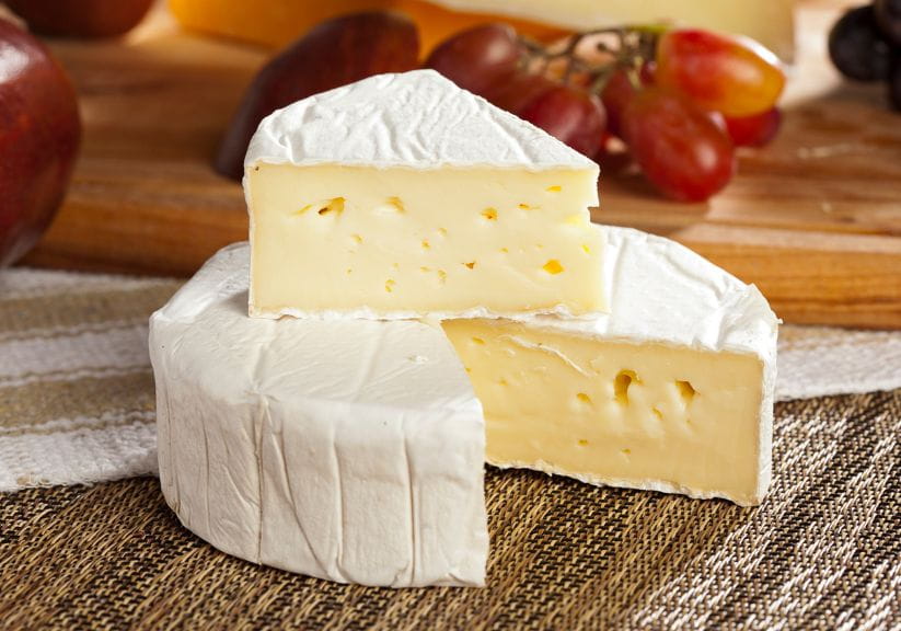 two brie cheeses both cut open on a wooden surface