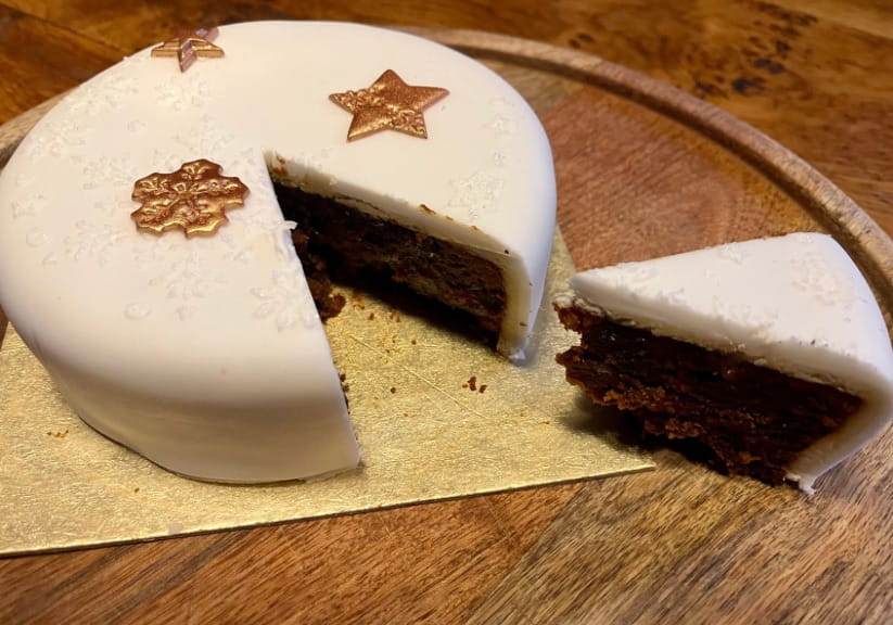 An Aldi Christmas cake on a plate with a slice cut out of it
