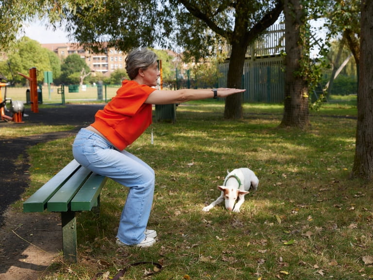 A woman doing a squat in the park during a workout with her dog