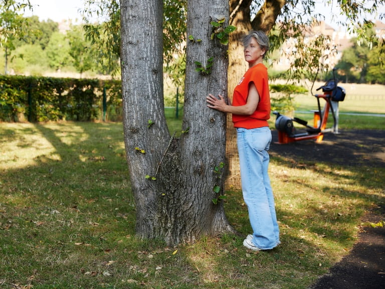 A woman doing calf raises while holding a tree for support in the park