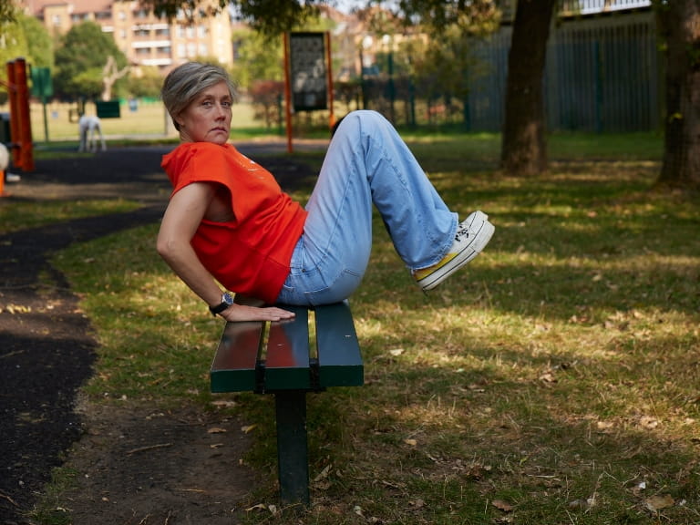 A woman doing a seated knee tuck on a park bench