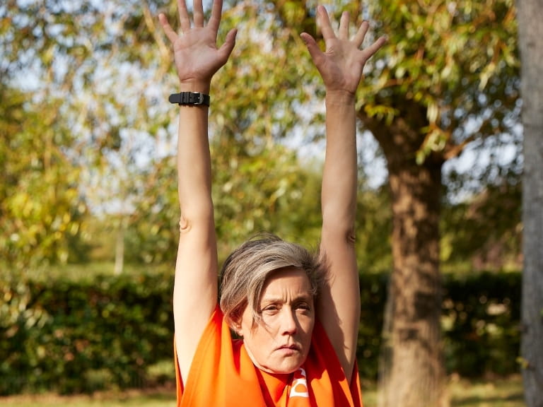 A woman doing a seated shoulder press on a park bench