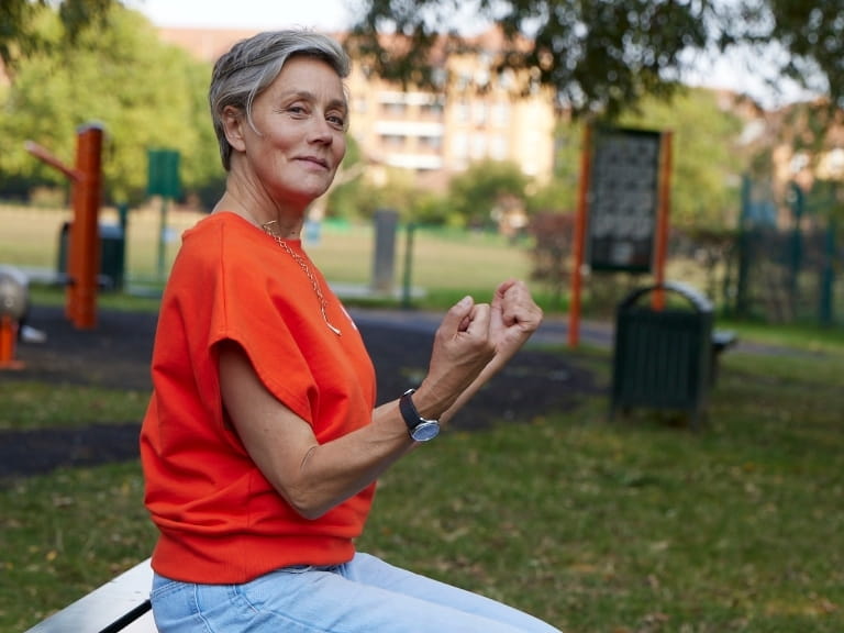 A woman doing a seated bicep curl on a park bench