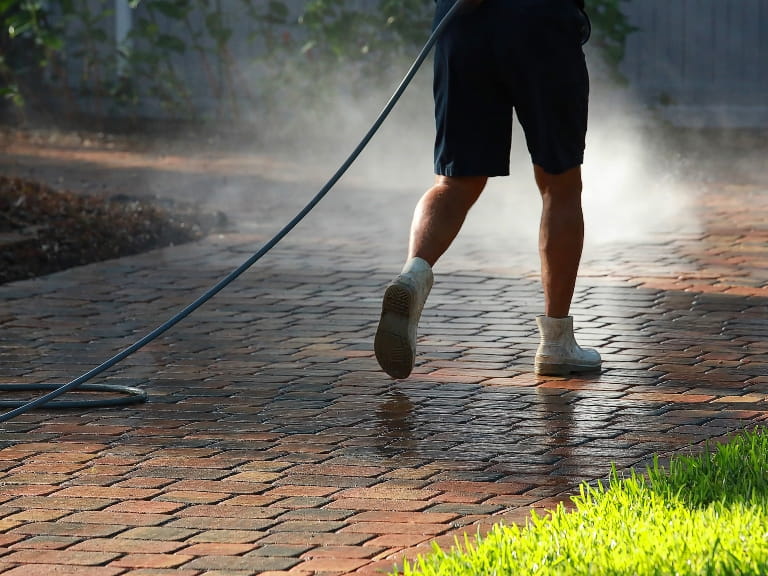 Someone in shorts pressure washing a block paved driveway