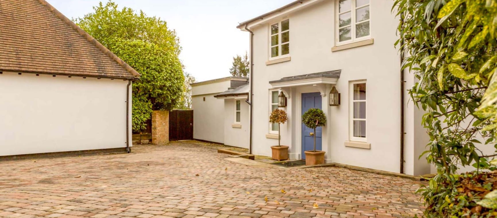 A white cottage with blue front door and block-paved driveway and garage