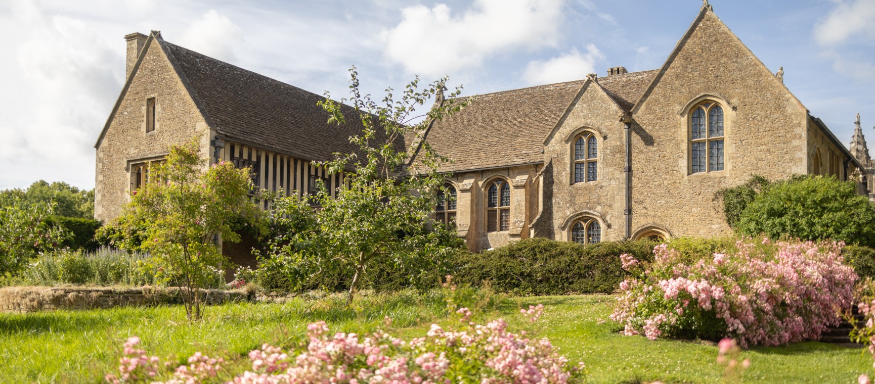 Great Chalfield Manor and garden on a sunny day with pink flowers blooming in the garden
