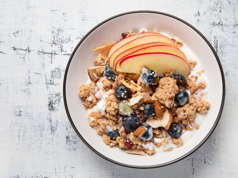 A bowl of nutty granola with yoghurt, blueberries and apple slices