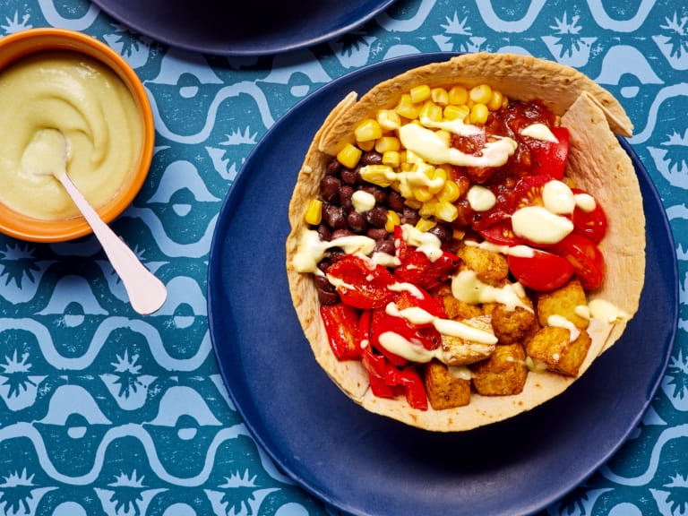 Vegan burrito bowl on a plate with a bowl of avocada crema on the side