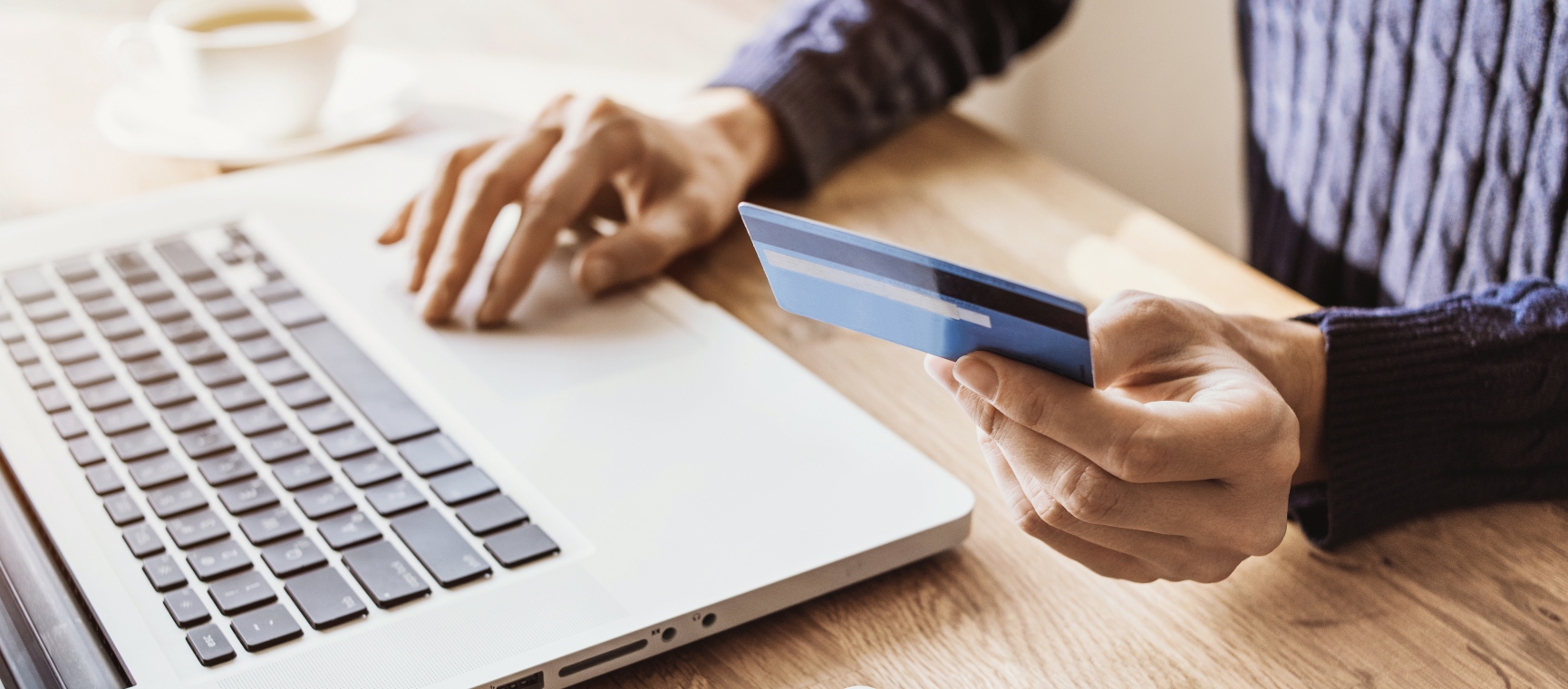 A person using a laptop and holding a bank card
