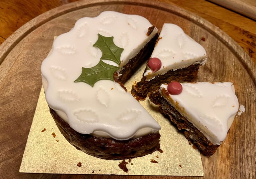An M&S Christmas cake on a wooden board with two slices cut