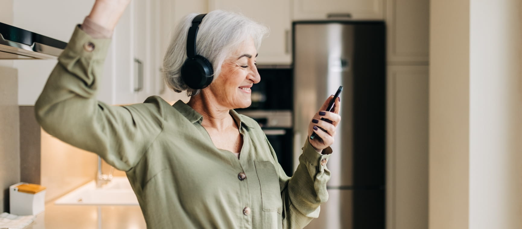 A senior woman dancing in the kitchen while listening to music through headphones