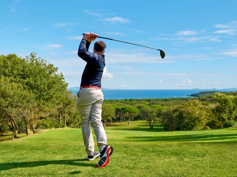 A professional golfer on an open green with tree on a sunny day