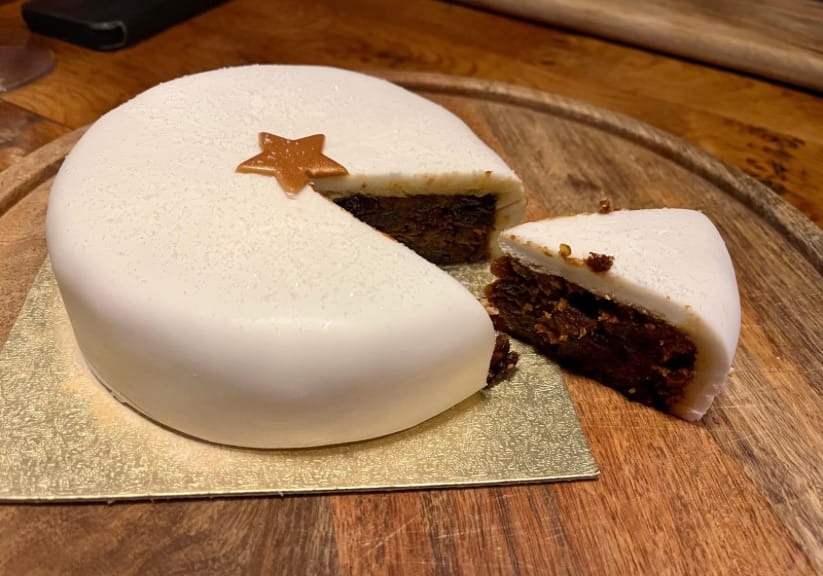 A Sainsbury's Christmas cake on a board with a slice cut out of it