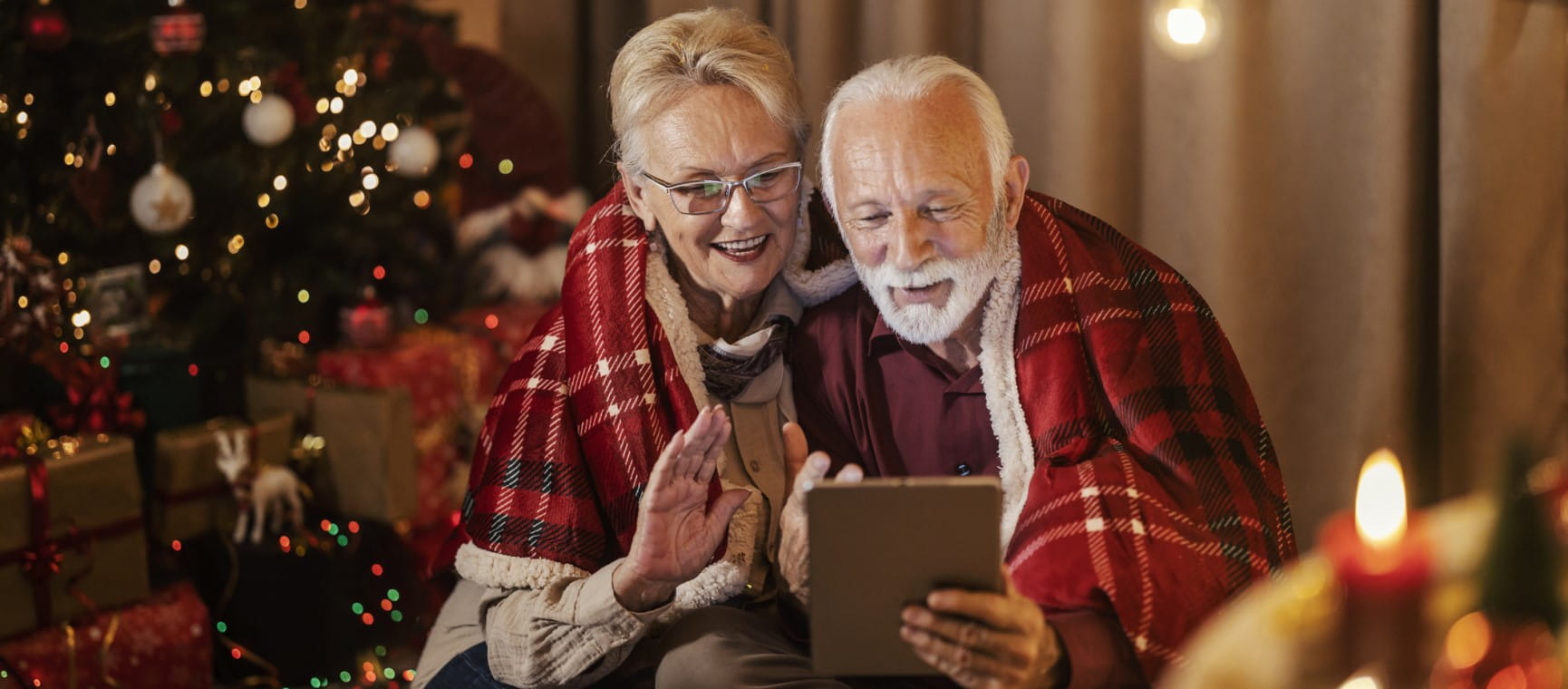 An older couple on a tablet in front of a christmas tree