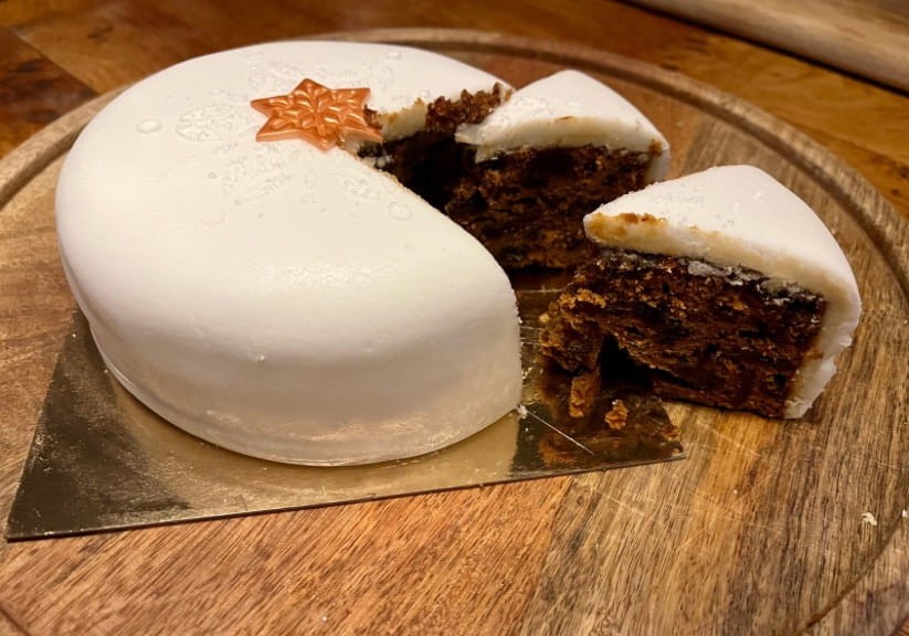 A Tesco Christmas cake on a wood board with a slice cut out