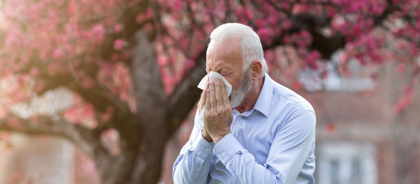 Man sneezing next to a big tree