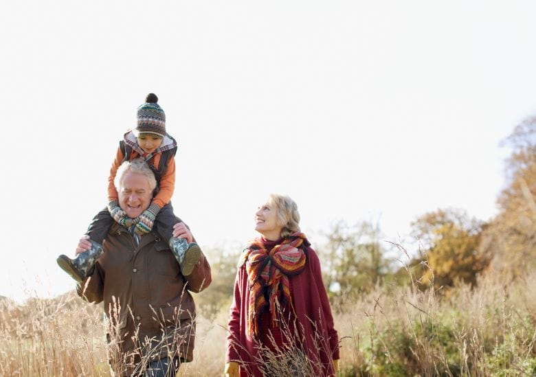 Grandparent couple walking through fields with a child on their shoulders
