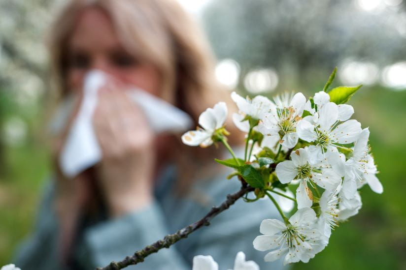 Woman sneezing with some flowers at the forefront