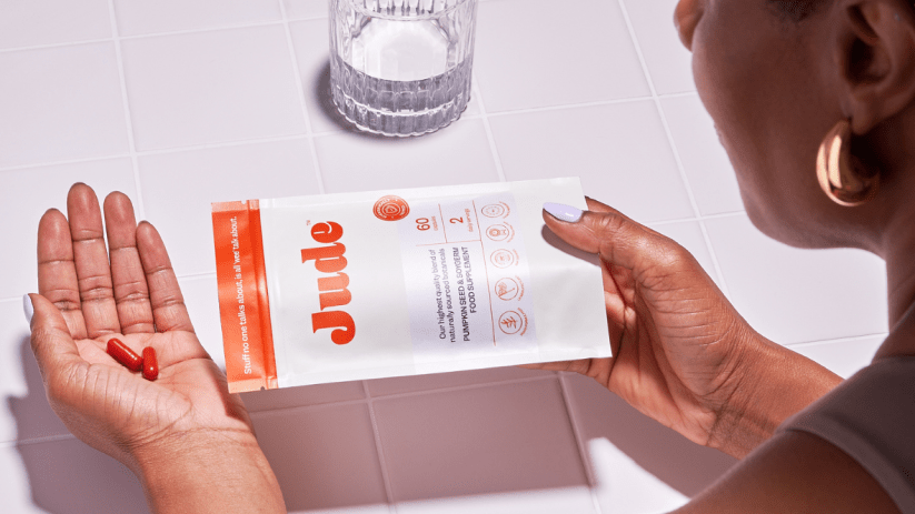 A woman shaking a capsule out of a packet of Jude bladder supplements