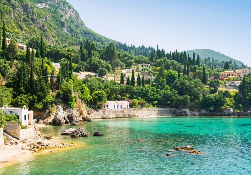 a cove in Corfu with a sandy beach and turquoise sea with green hills behind in the sunshine