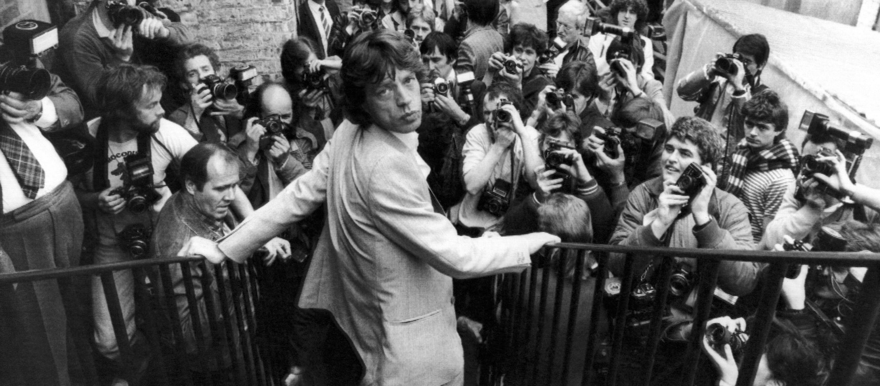 Mick Jagger of the Rolling Stones standing on a staircase in front of a crowd of people taking photographs | Alamy