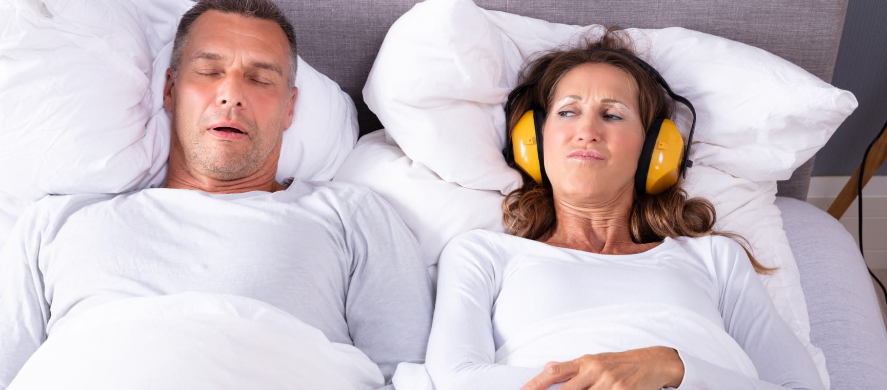 Two people in bed, one is snoring the other is wearing ear defenders | Getty/AndreyPopov