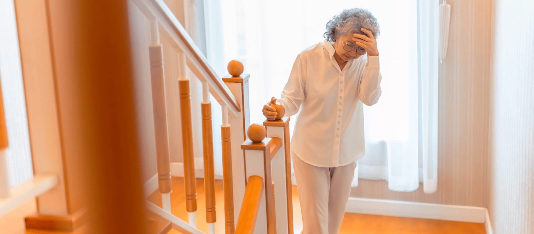 A woman standing on a staircase holding her head looking dizzy