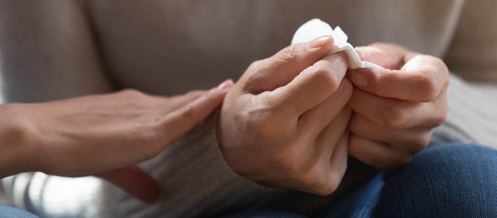 A close up shot of hands, one person consoling another holding tissues | Getty