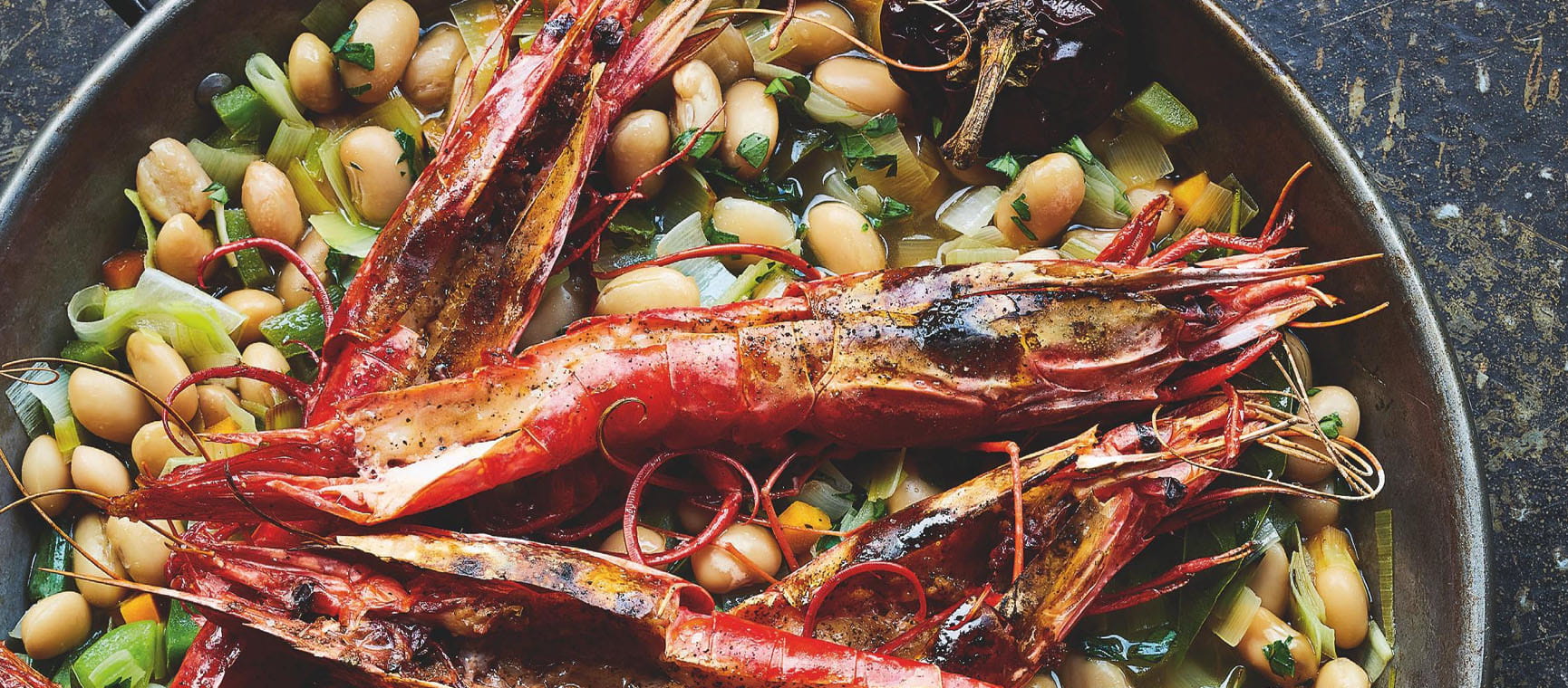 Prawns on a bed of beans in a skillet