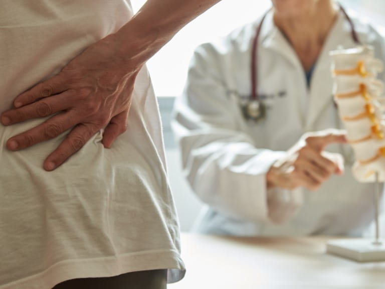 A male doctor explaining lumbar anatomy to female patient complaining of back pain at medical clinic | Getty