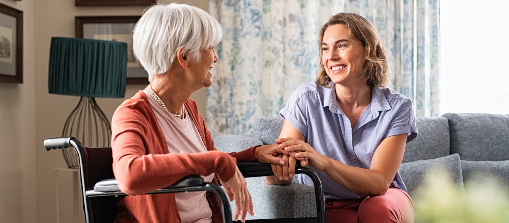 Cheerful woman talking to older woman in wheelchair at carehome | Getty/Ridofranz