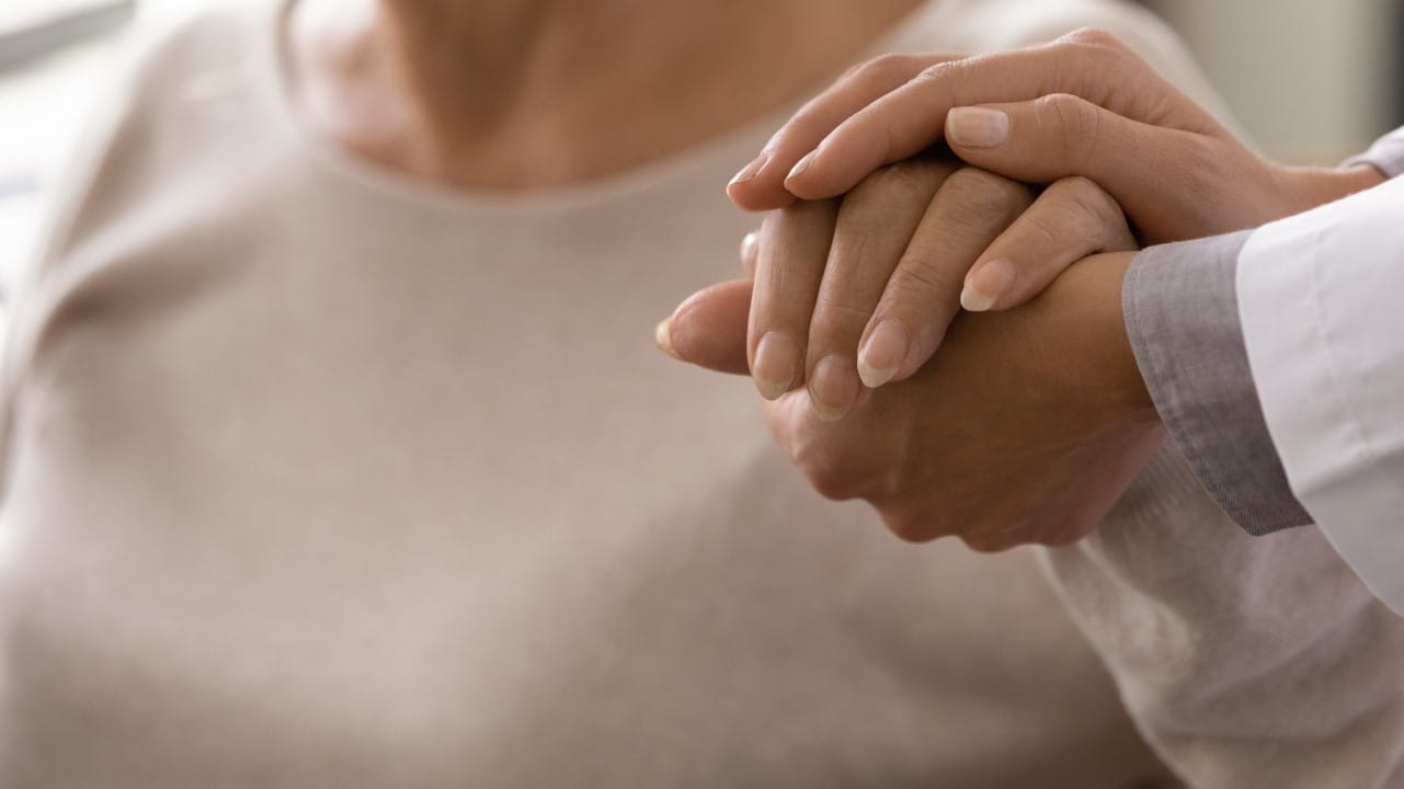 An older person with their hand being held reassuringly by a medical professional
