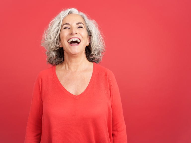 Studio portrait with red background of a mature woman in red shirt laughing while standing | Getty/Ramon Ivan Moreno Prieto