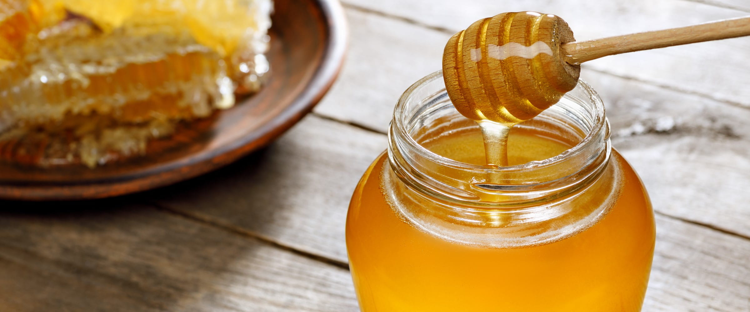 Honey pouring from dipper in glass jar and honeycomb on wooden table | Getty/Alter_photo