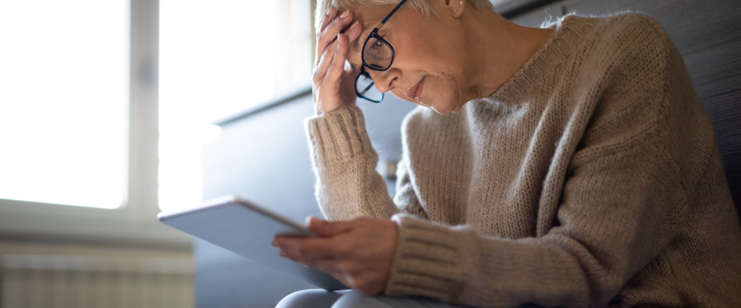 An older woman looks anxiously at her tablet