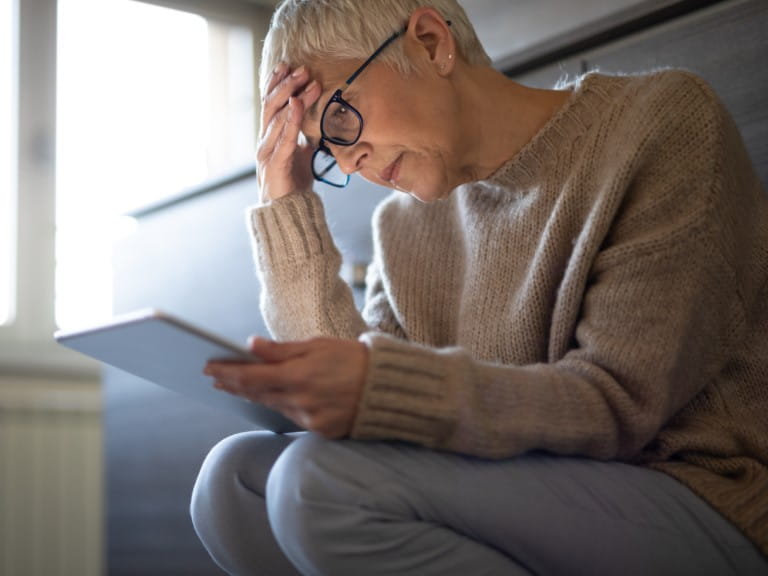 An older woman looks anxiously at her tablet