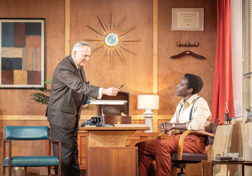 Two actors either side of the desk looking intently