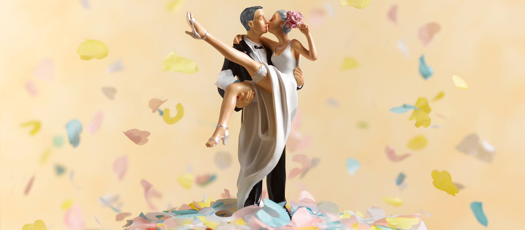 A model of a bride and groom on top of a wedding cake with confetti