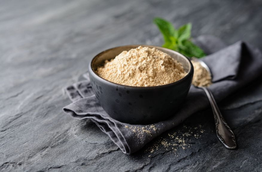 Maca root powder in a bowl and spoon on stone background