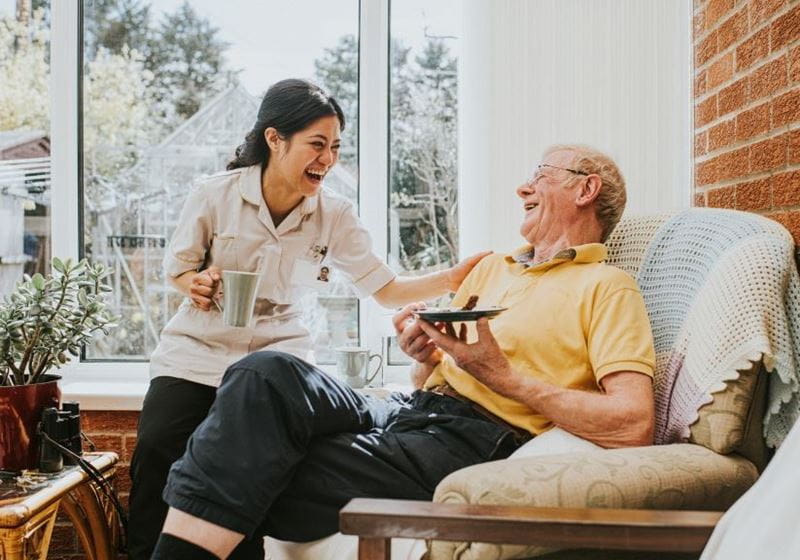 A friendly, young, female carer visits an elderly male in his home.