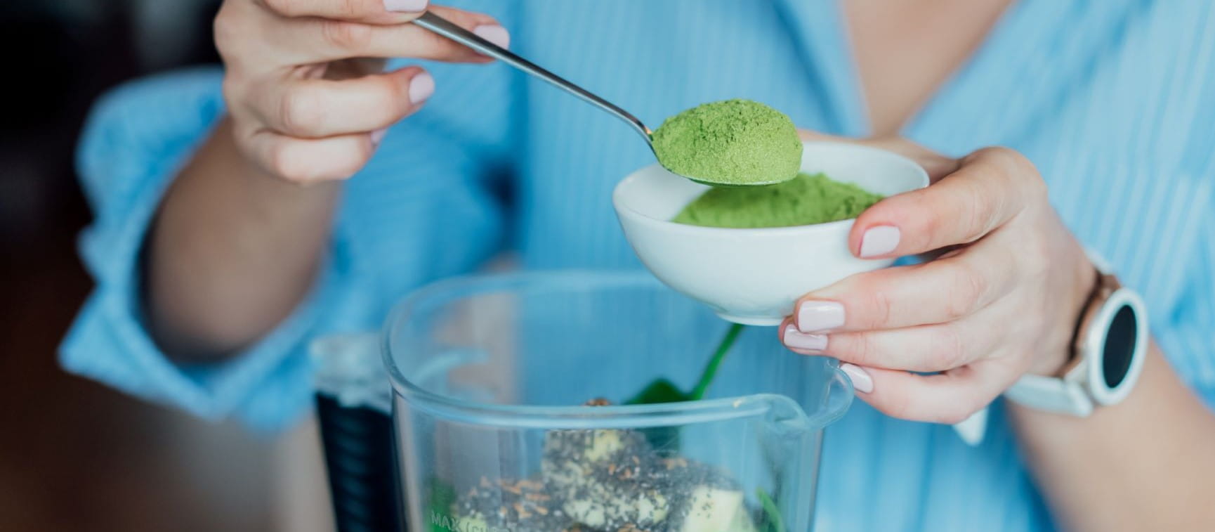 Close up woman adding wheat grass green powder during making smoothie on the kitchen. Superfood supplement