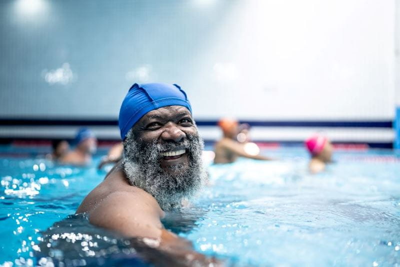 Man in a swimming pool looking jolly in his swimming hat