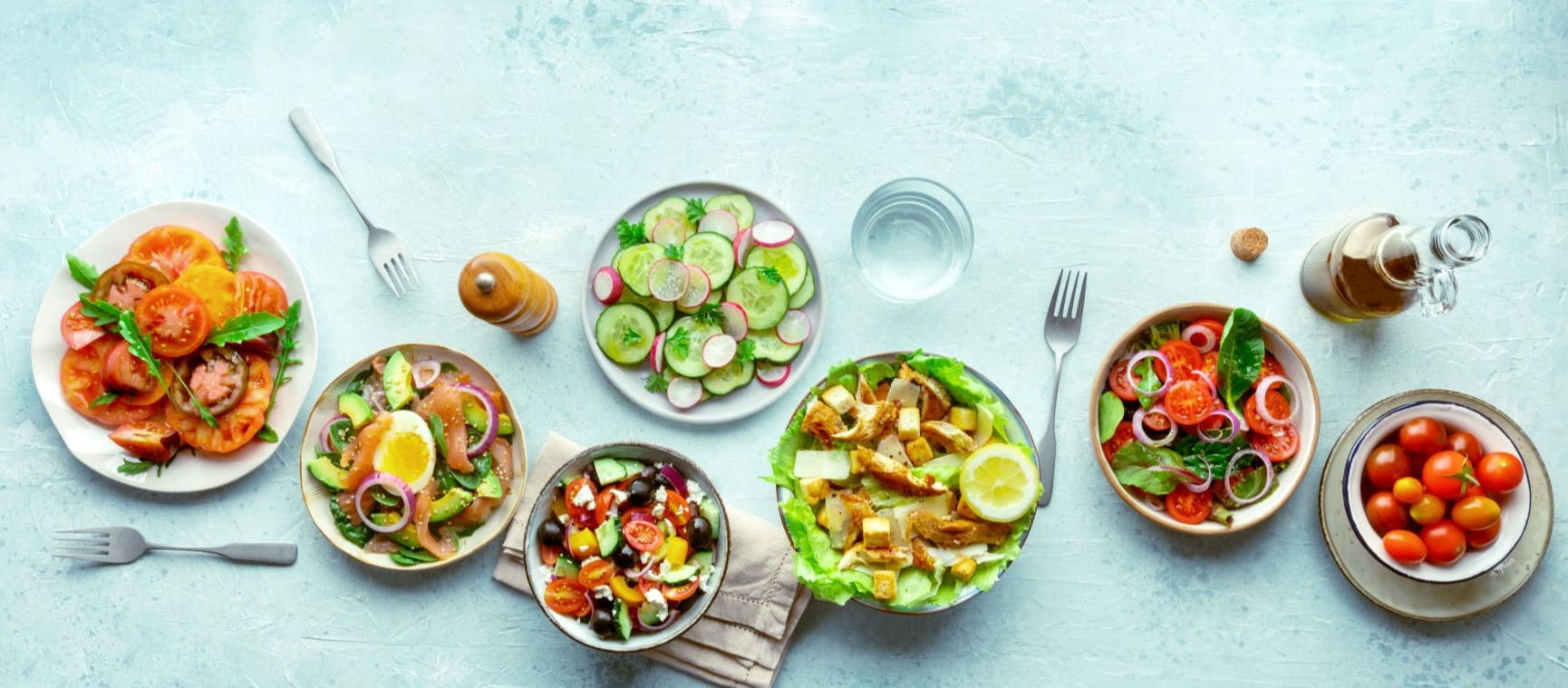 Fresh salads, overhead flat lay shot of an assortment. Variety of plates and bowls with green vegetables