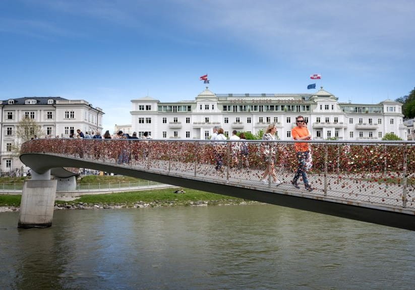 People walk on the Marko Feingold pedestrian bridge, with all the love locks attached, crossing the Salzach river in Salzburg