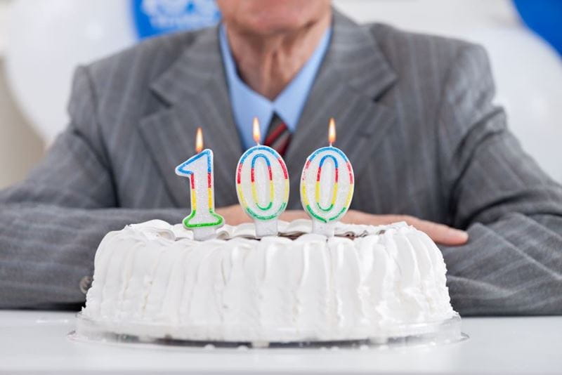 a man behind a birthday cake with 100 on top of it