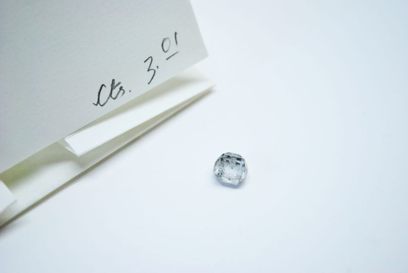 A CVD HPHT lab grown rough solitaire diamond next to tweezers and certification