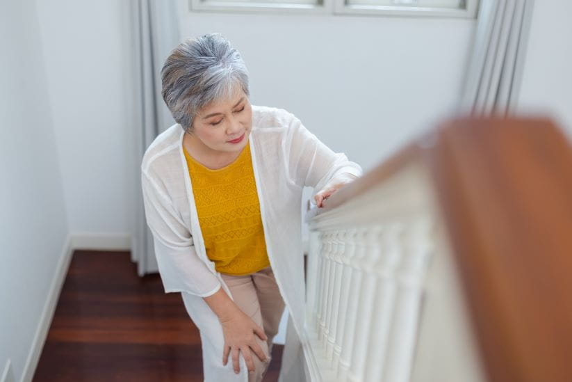 Woman holding her knee in pain while climbing the stairs